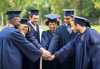 Image showing happy students in mortar boards with hands on top