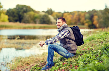 Image showing smiling man with backpack resting on river bank