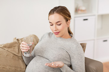 Image showing happy pregnant woman with water and pills at home