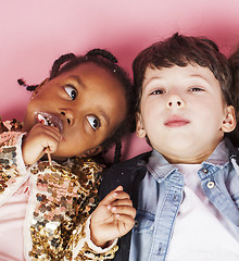 Image showing little cute caucasian boy and african american girl hugging playing on pink background, happy smiling diverse nation and age children, lifestyle people concept close up