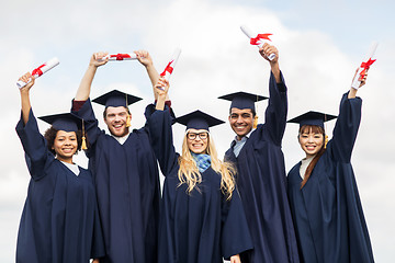 Image showing happy students in mortar boards waving diplomas