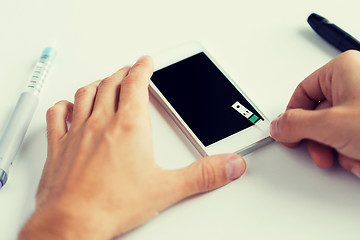 Image showing close up of man with smartphone making blood test