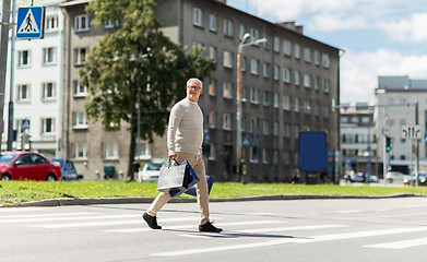 Image showing senior man with shopping bags walking on crosswalk