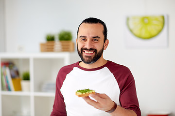 Image showing man eating avocado sandwiches at home kitchen