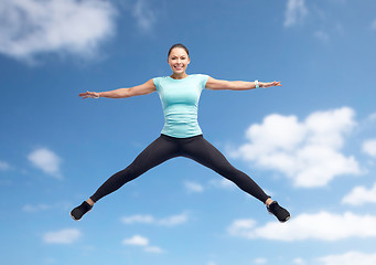 Image showing happy smiling sporty young woman jumping in air