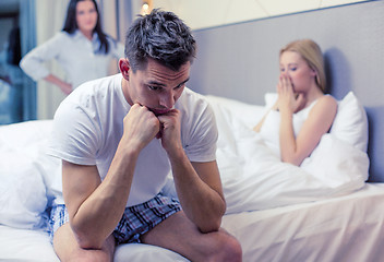 Image showing man sitting on the bed with two women on the back