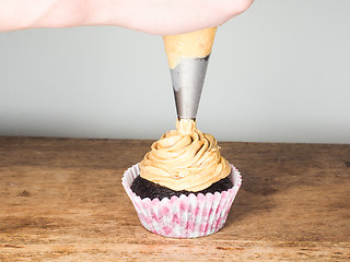 Image showing Professional cake baker applying frosting onto a chocolate cupca