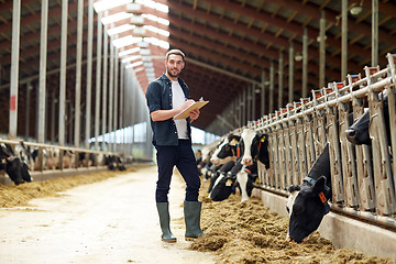 Image showing farmer with clipboard and cows in cowshed on farm