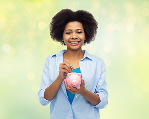 Image showing happy african woman putting coin into piggy bank