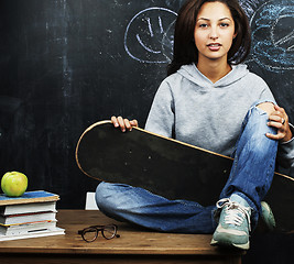 Image showing young cute teenage girl in classroom at blackboard seating on ta