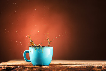 Image showing Brown splashes out drink from cup of tea on a brown background