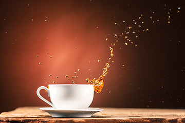 Image showing Brown splashes out drink from cup of tea on a brown background