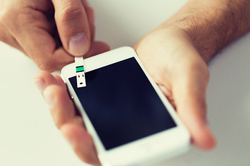 Image showing close up of man with smartphone making blood test