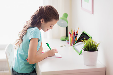 Image showing girl with tablet pc writing to notebook at home