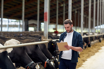 Image showing farmer with clipboard and cows in cowshed on farm