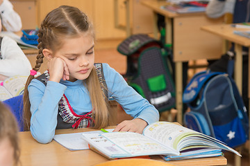 Image showing A girl pupil in the classroom at school looking at a textbook