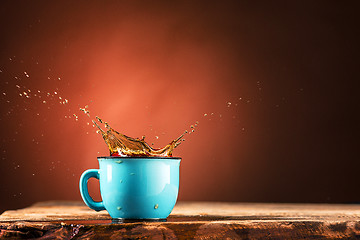 Image showing Brown splashes out drink from cup of tea on a brown background