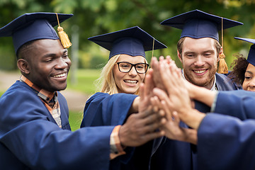 Image showing happy students in mortar boards making high five