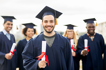 Image showing happy students in mortar boards with diplomas