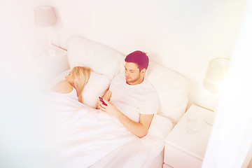 Image showing man texting message while woman is sleeping in bed