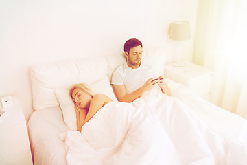 Image showing man texting message while woman is sleeping in bed