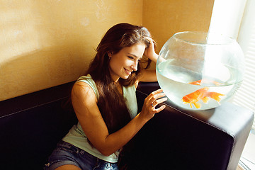 Image showing pretty woman playing with goldfish at home, sunlight morning