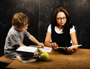 Image showing little cute boy with young teacher in classroom studying at blac