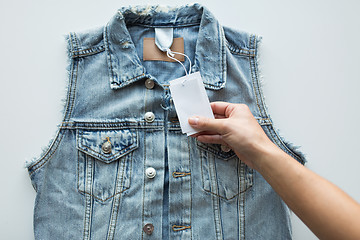 Image showing close up of hand holding price tag of denim vest