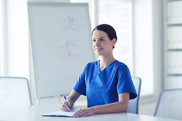 Image showing happy female doctor or nurse writing to clipboard