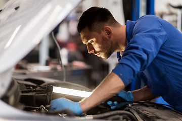 Image showing mechanic man with lamp repairing car at workshop