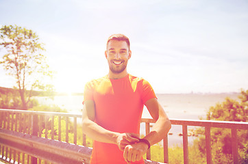 Image showing smiling young man with smart wristwatch at seaside