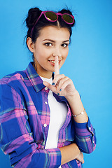 Image showing young pretty teenage modern hipster girl posing emotional happy smiling on blue background, lifestyle people concept 