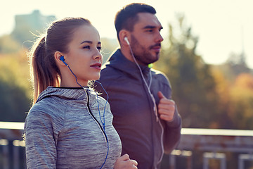 Image showing happy couple with earphones running in city