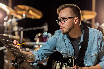 Image showing man with guitar writing to music book at studio