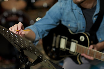 Image showing man with guitar writing to music book at studio