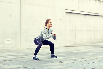 Image showing happy woman doing squats and exercising outdoors