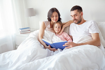 Image showing happy family reading book in bed at home