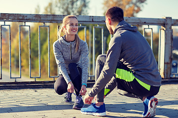 Image showing smiling couple tying shoelaces outdoors