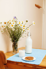 Image showing Simply stylish wooden kitchen with bottle of milk and glass on table, summer flowers camomile, healthy foog moring concept
