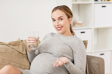 Image showing happy pregnant woman with water and pills at home