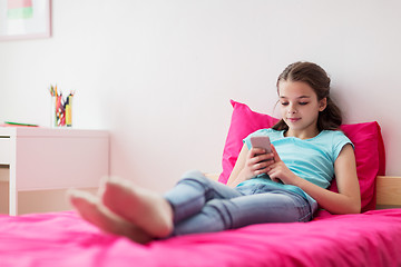 Image showing smiling girl texting on smartphone at home