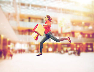 Image showing smiling young woman with shopping bags jumping