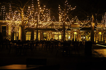 Image showing empty night restaurant, lot of tables and chairs with noone, magic fairy lights on trees like christmas celebration
