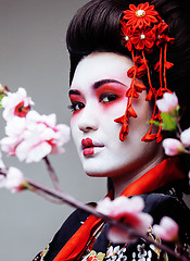 Image showing young pretty geisha in black kimono among sakura, asian ethno close up