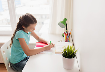 Image showing happy girl with book writing to notebook at home