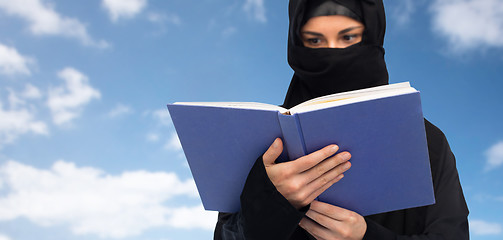 Image showing muslim woman in hijab reading book over sky