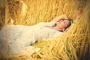 Image showing smiling woman in white dress lying among the ears of wheat