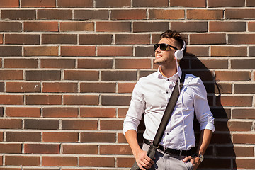 Image showing young man in headphones with bag over brickwall