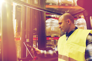 Image showing man with tablet pc operating forklift at warehouse