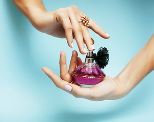 Image showing woman hands holding bottle of perfume pink manicure and jewelry on blue background, luxury concept